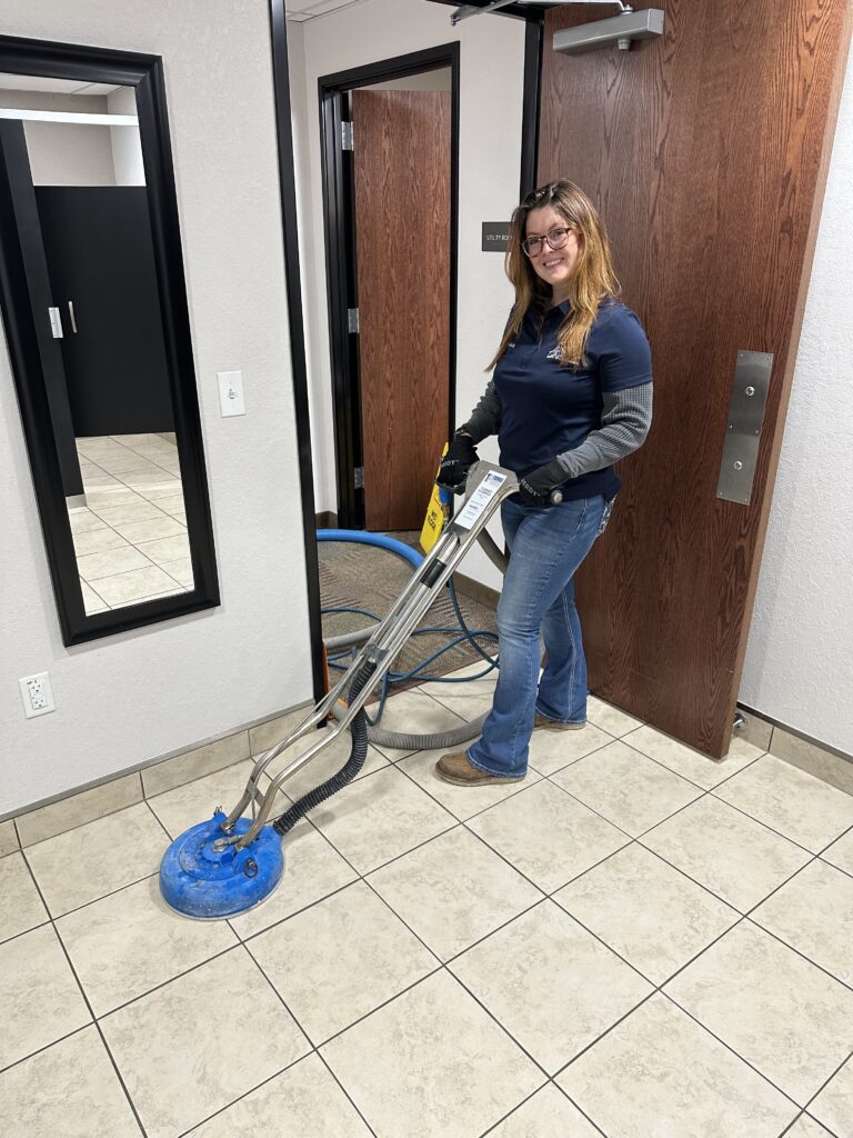 IMG_20260129_225529 - Elite Carpet, Tile & Grout Clean Elite technician running a sealed spinner tool across a commercial tile floor, with the vacuum hose and hot water line trailing behind
