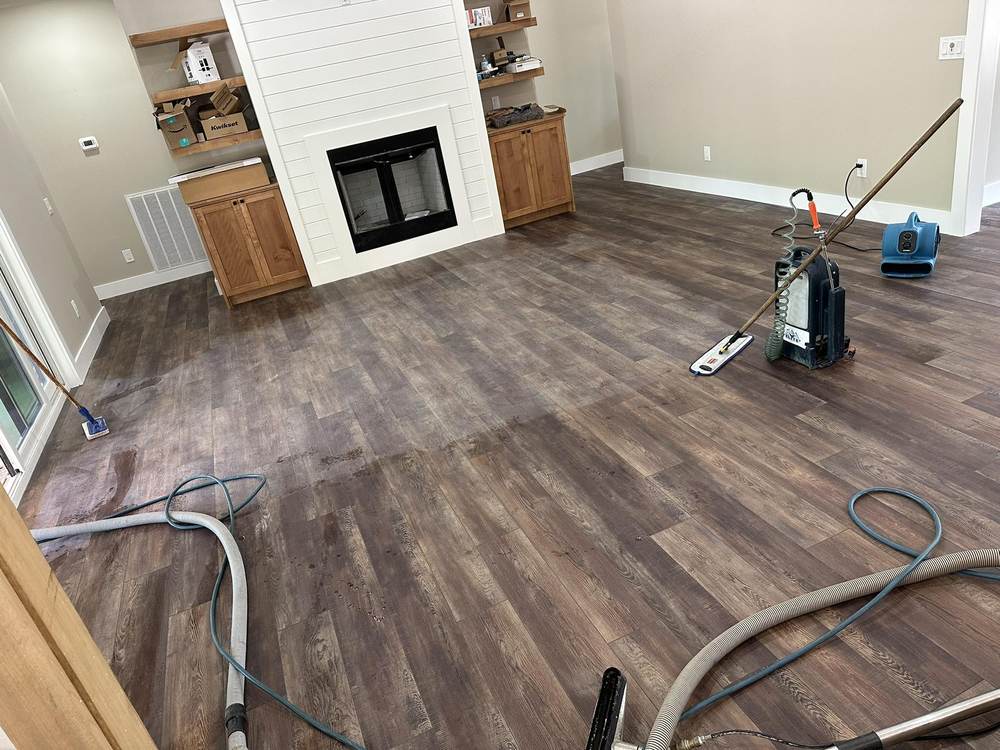 Luxury vinyl plank living room mid-job, with two microfiber flat mops, an Elite portable sprayer, an air mover and extraction hoses on the floor
