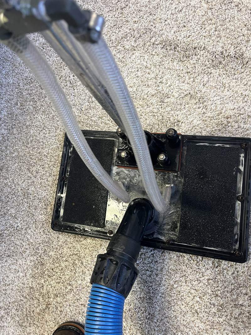 Water claw extraction tool pressed onto a carpet spot, with clear hoses pulling the water back out